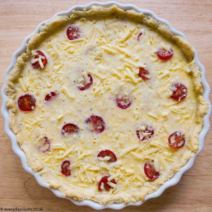 An uncooked Tuna and Tomato Quiche in a white china flan dish