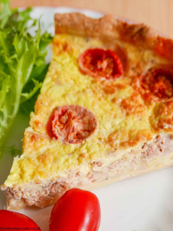 A slice of Tuna and Tomato Quiche on a white plate, with lettuce and tomato