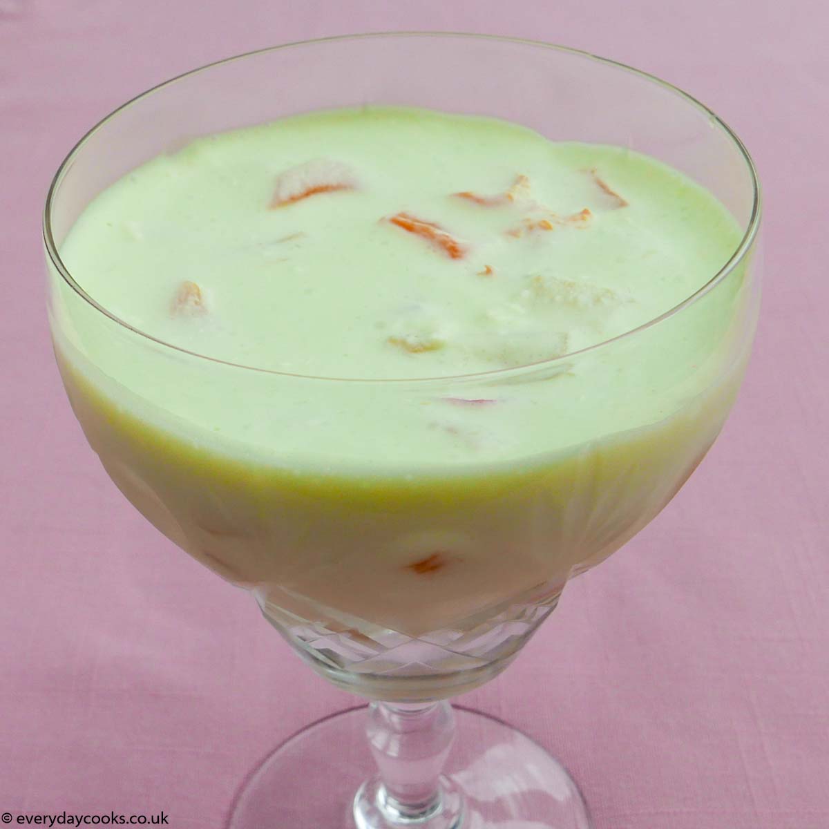 Lime fruit dessert in a cut glass goblet, It stands on a small plate patterned with flowers., with a fruit spoon, on a pink tablecloth.