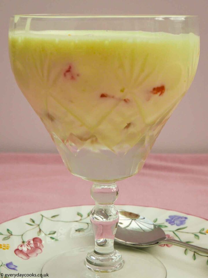 Lime fruit dessert in a cut glass goblet, It stands on a small plate patterned with flowers., with a fruit spoon, on a pink tablecloth.