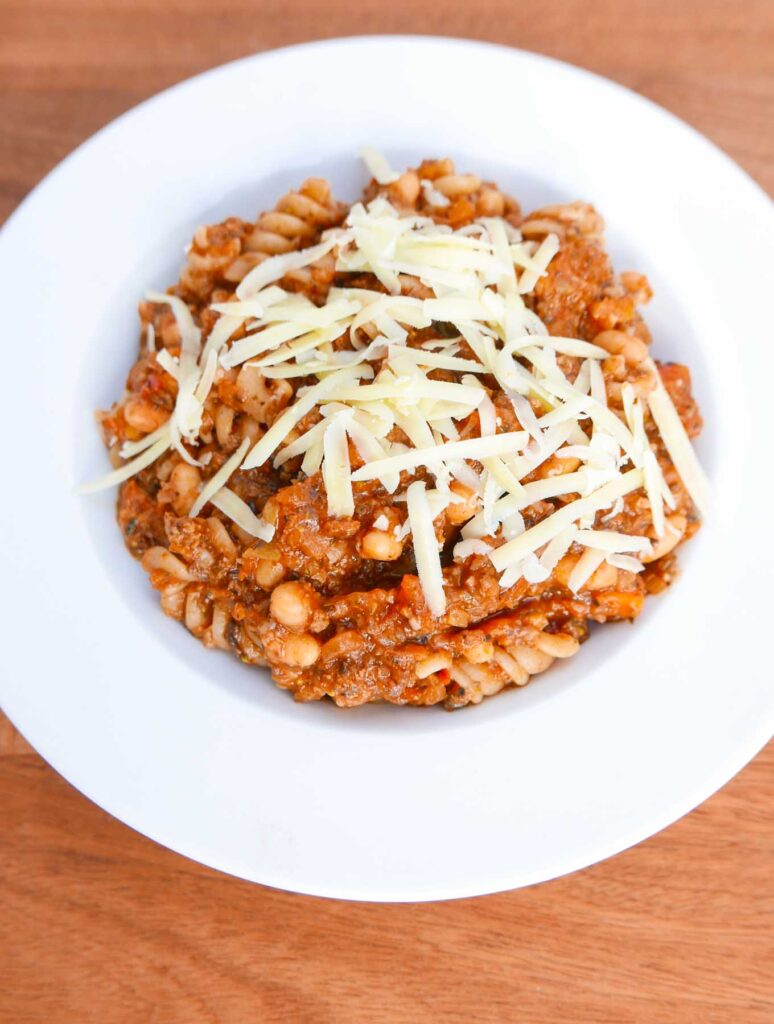 Cowboy dinner - a mince, vegetable and pasta dish with baked beans in a white china bowl with grated cheese.