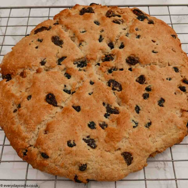 A whole fruit tea scone cooling on a wire rack on a marble kitchen worktop.