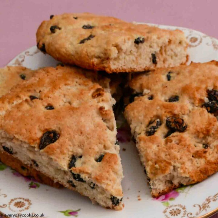 Slices of fruit tea scone on a large plate with a fluted gold edge and a pattern of pink roses, sitting on a pink tablecloth.