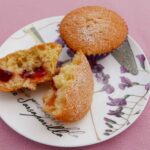 Two jammy buns on a small flowered plate. One bun is split open to see the strawberry jam inside.