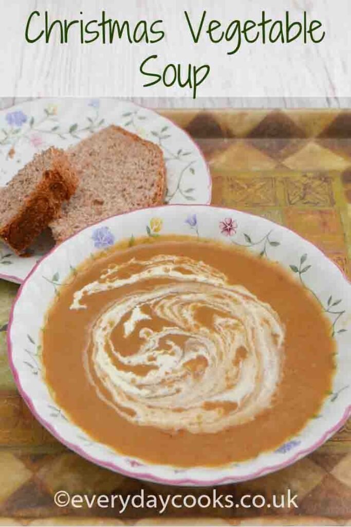 Christmas vegetable soup with a swirl of cream in a bowl with a piece of bread on a plate.