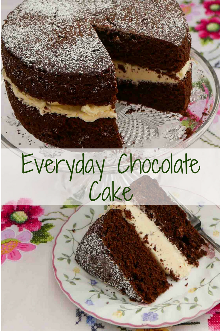 Large everyday chocolate cake with vanilla buttercream filling on a glass cake stand with a slice removed. on a glass cake stand, with a slice on a plate