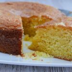 A large Lemon Drizzle Cake with a slice cut to show the moist centre