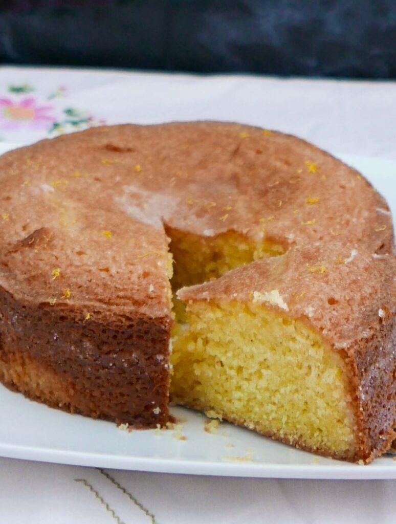 A lround Lemon Drizzle Cake with a slice cut to show the lemon-soaked centre