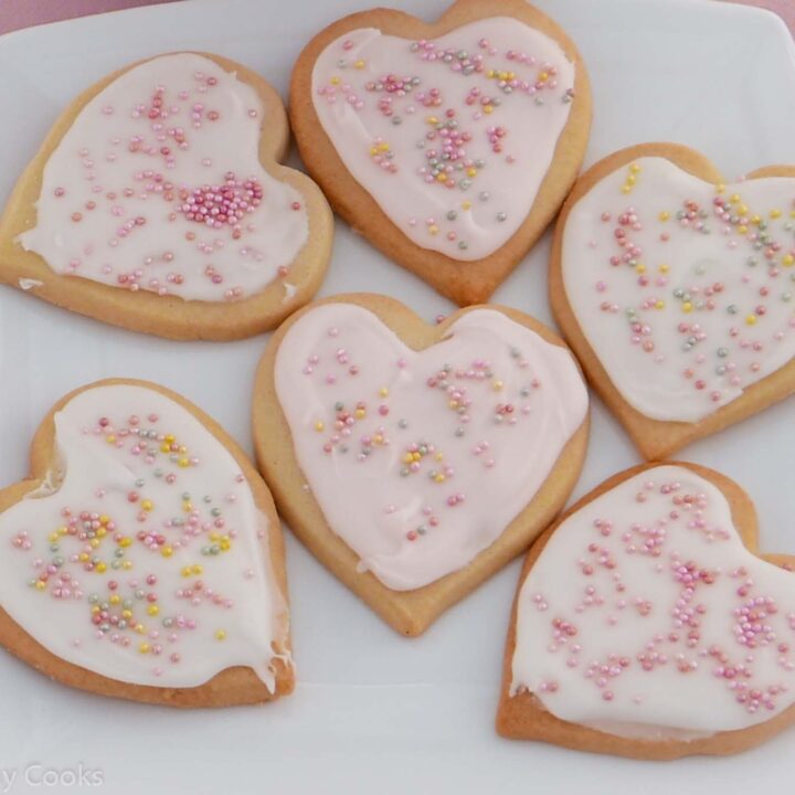 Heart-shaped Valentine biscuits with white or pale pink icing and pink, gold and silver sprinkles