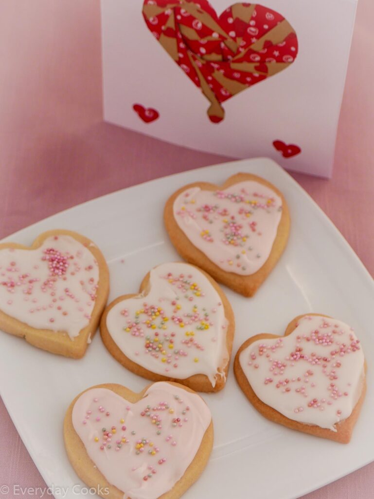 Heart-shaped Valentine biscuits with white or pale pink icing and pink, gold and silver sprinkles