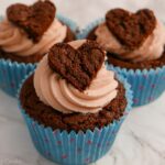 3 easy valentine cupcakes in a line. Chocolate flavour with pink buttercream and a heart on top