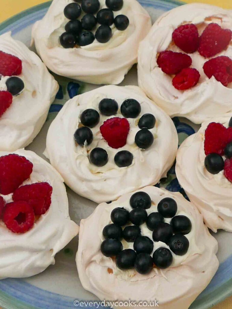 7 Pavlova nests, filled with cream, raspberries and blueberries, on a plate