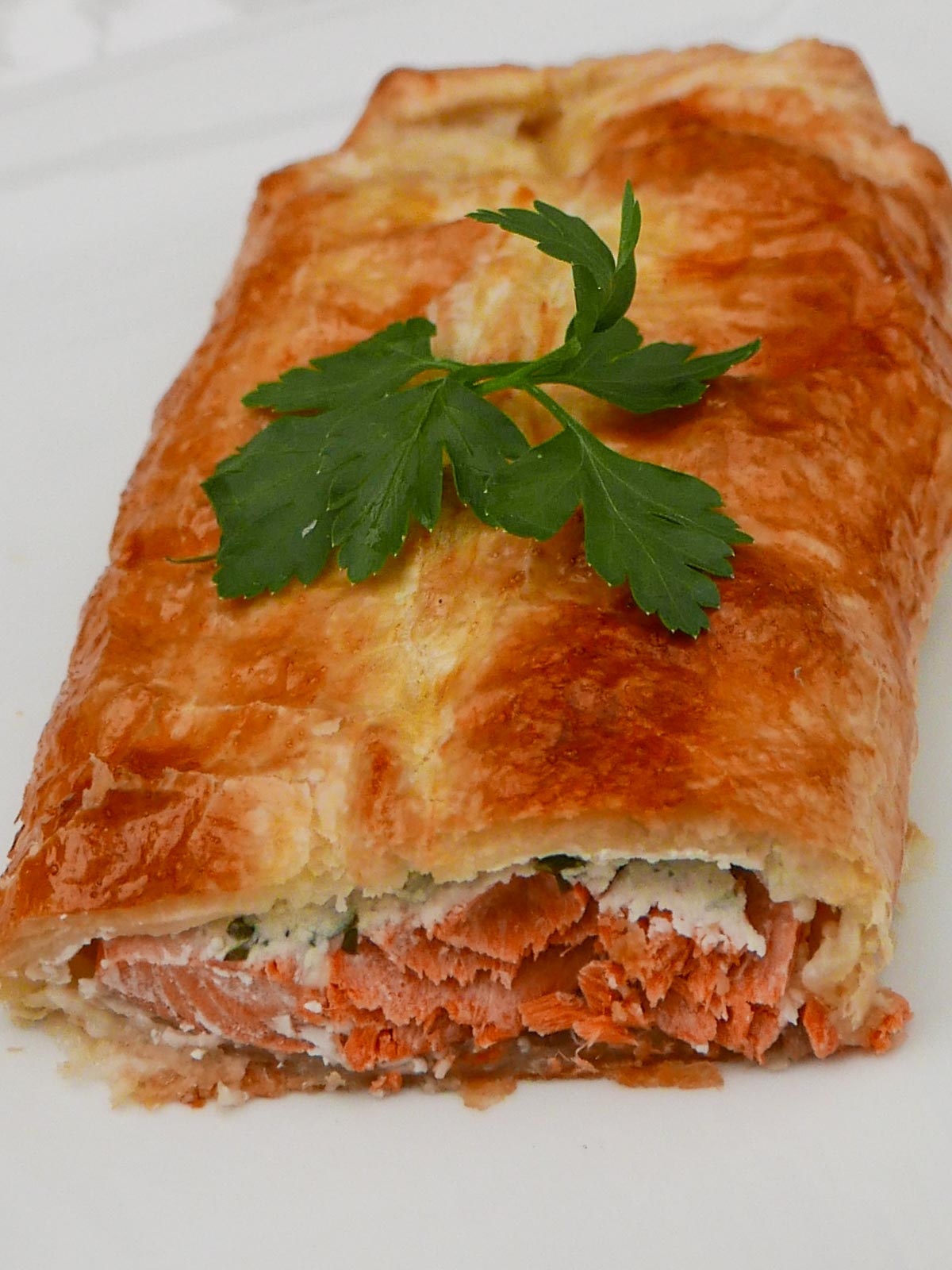 Salmon en Croûte - cut to show salmon baked in puff pastry with a parsley garnish.