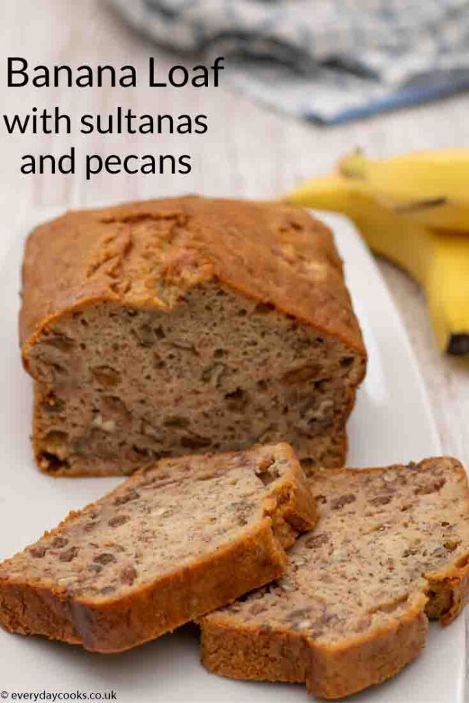 Two slices of Banana Loaf on a white plate with the rest of the cake and 2 bananas in the background