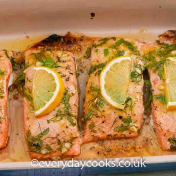 Four fillets of Baked Lemon Salmon garnished with slices of lemon and herbs in a gratin dish