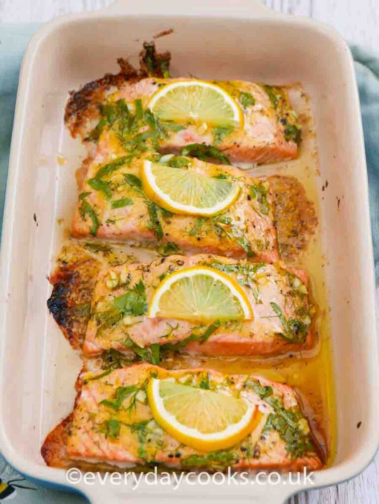 Four fillets of Baked Lemon Salmon garnished with slices of lemon and herbs in a gratin dish