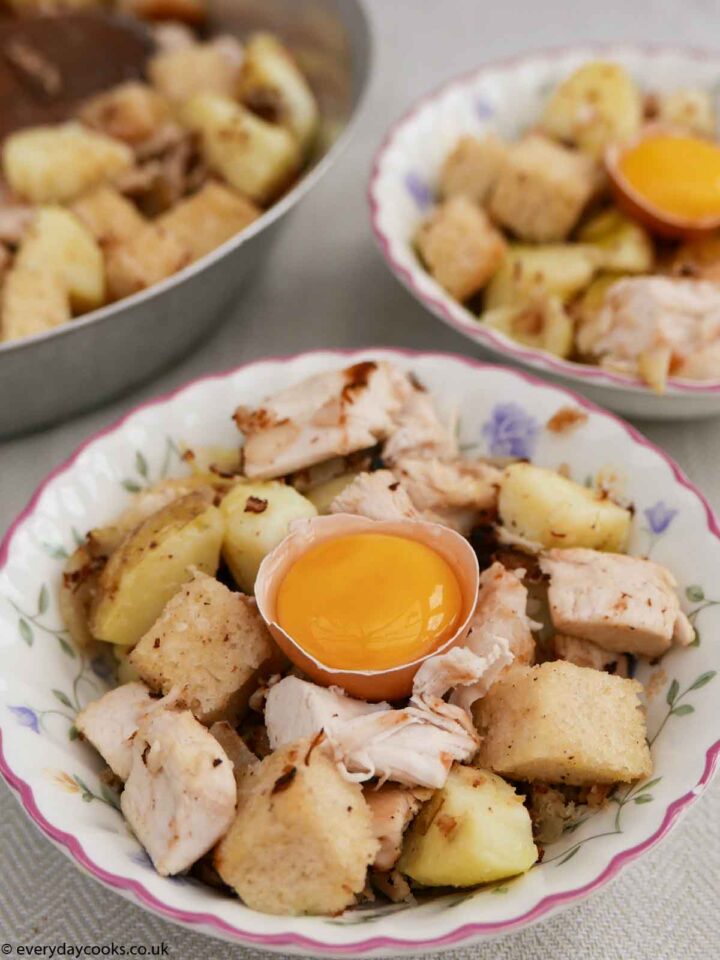 Pytt i panna with an egg yolk in the shell ready to eat. The pan of cooked food in the background right