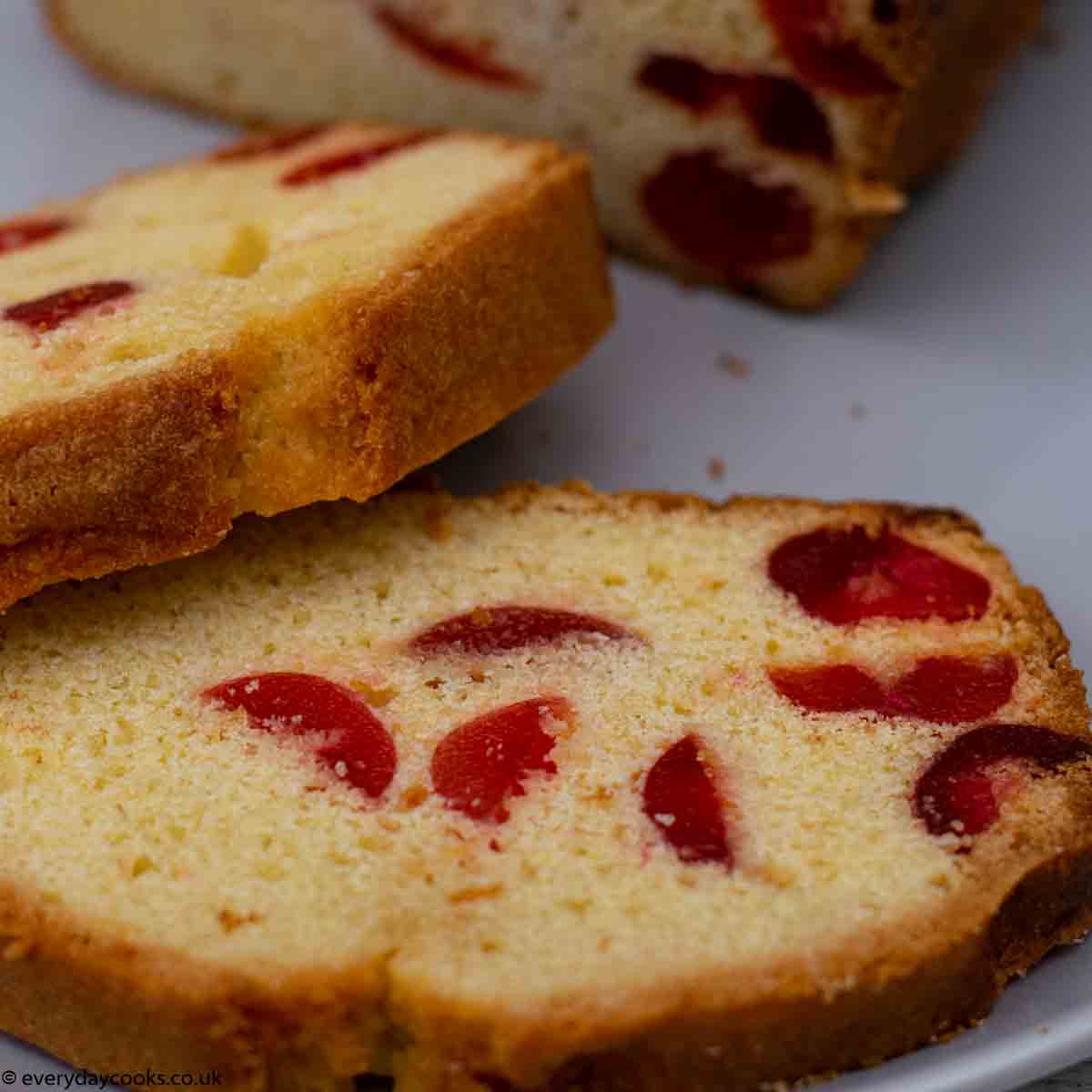 Slices of cherry cake on a grey plate with the rest of the cake in the background.