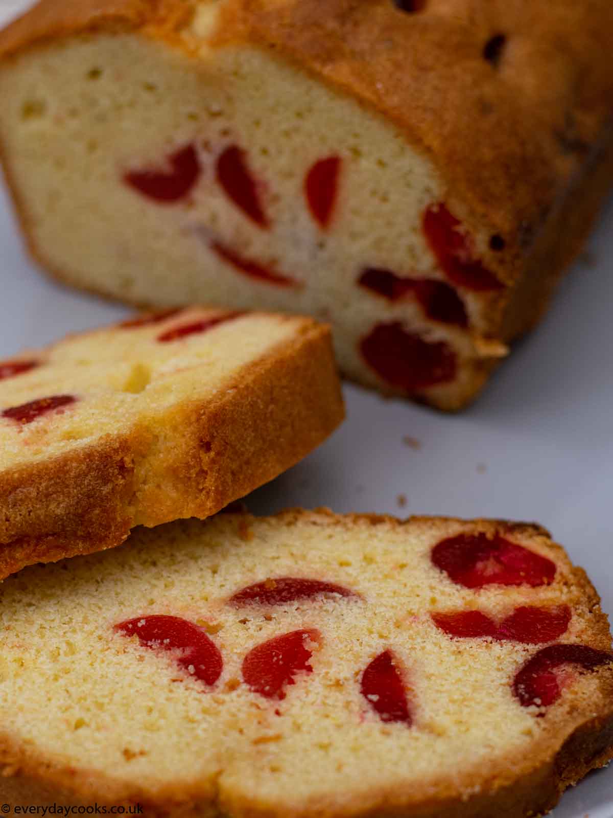 Slices of cherry cake on a grey plate with the rest of the cake in the background.