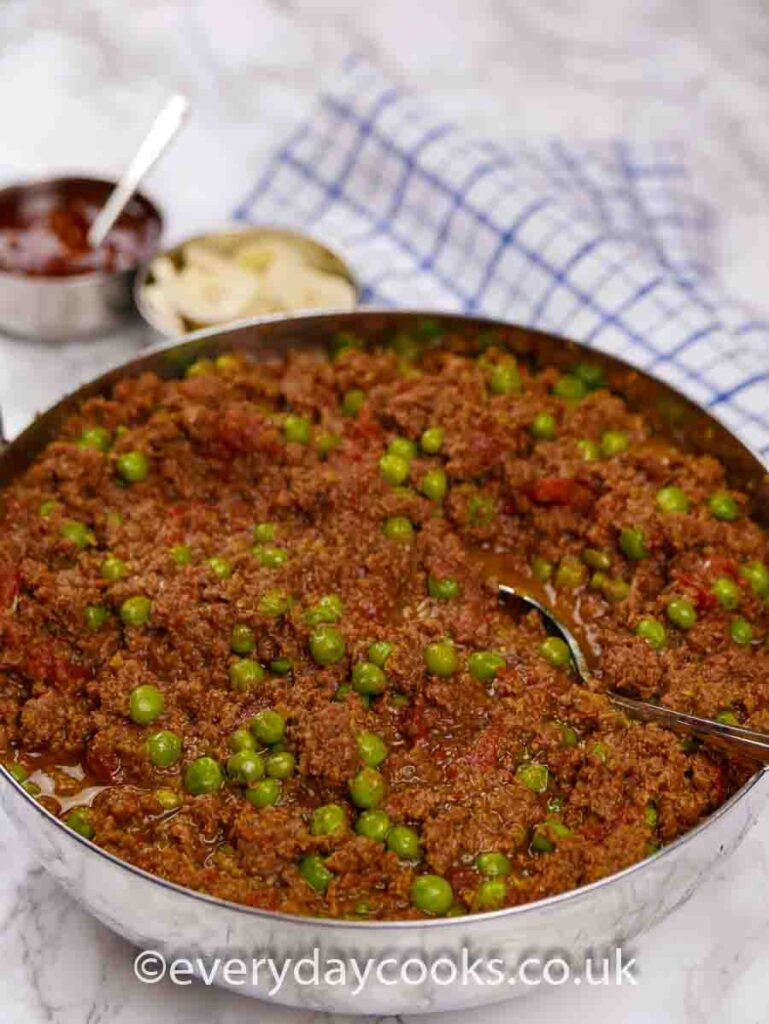 Keema in a stainless steel serving dish with Indian condiments