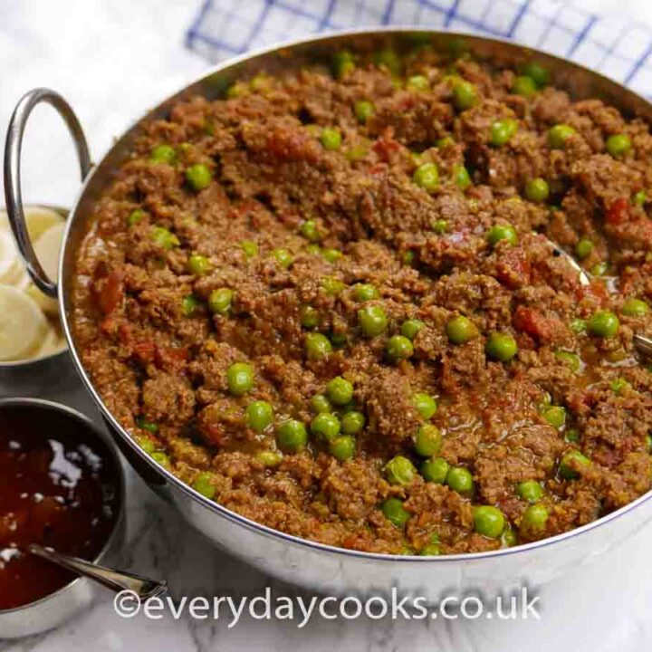 Keema in a stainless steel serving dish with Indian condiments