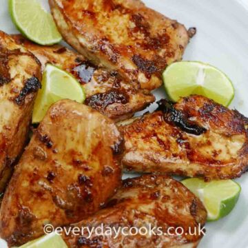Pieces of Ginger Lime Chicken in a white dish with a quartered lime