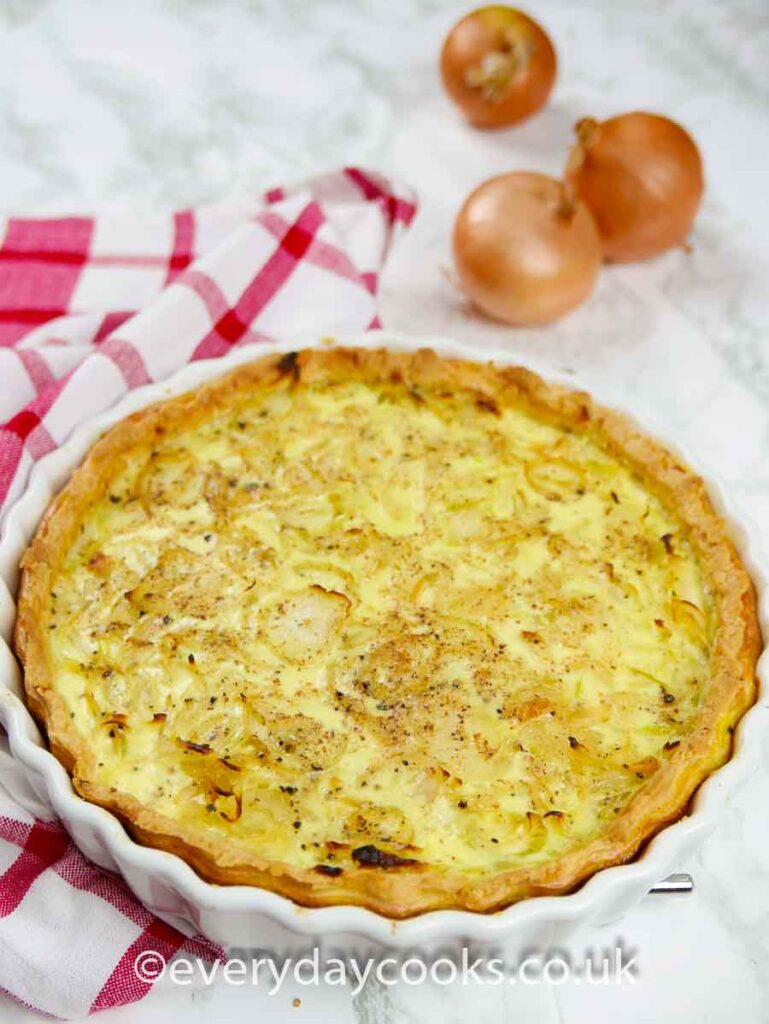 Onion Quiche in a china flan dish with onions in the background.