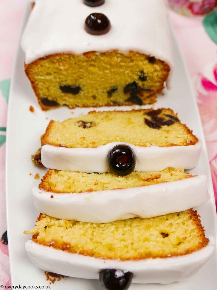 Iced Cherry Cake with a slice cut, on a white plate.