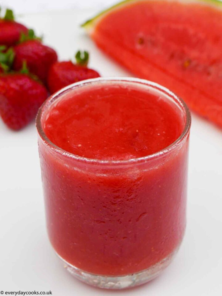 Frozen Watermelon Strawberry Smoothie in a short glass with a slice of watermelon and scattered strawberries.