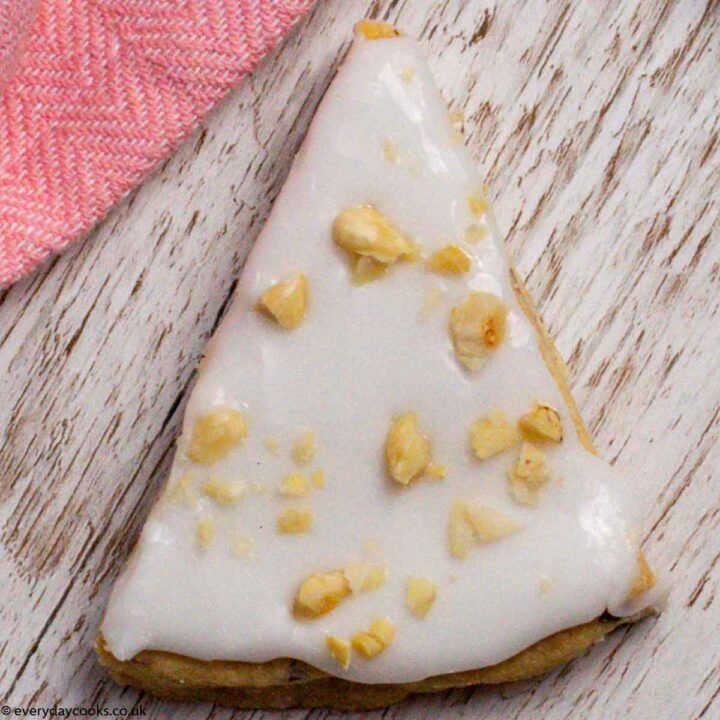 A slice of iced Almond Shortbread on a board next to a pink cloth