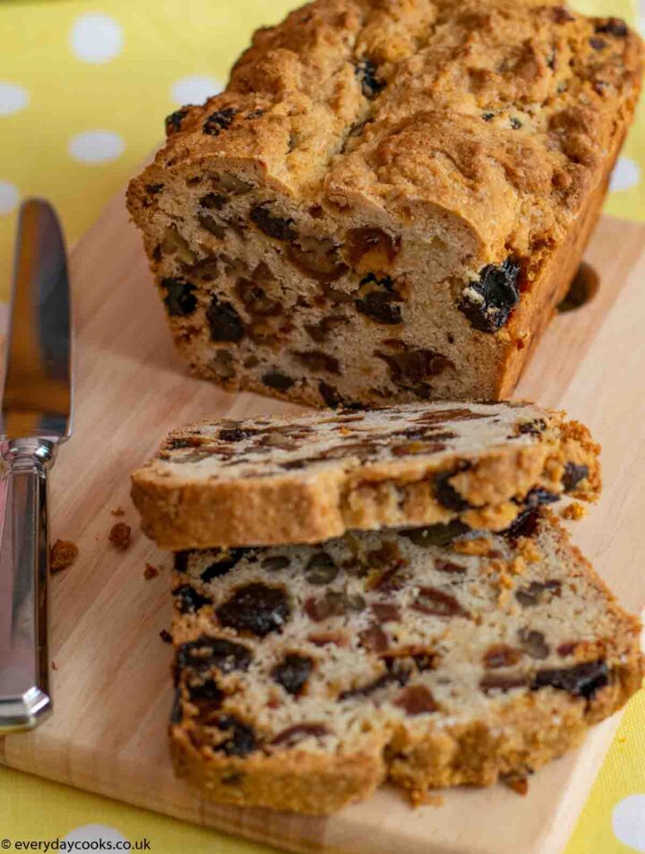 A cut Date and Walnut Loaf with 2 slices on a wooden board