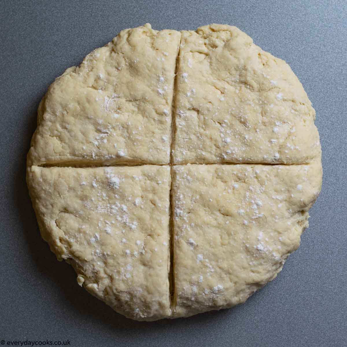 Dough flattened and scored with a cross ready for baking