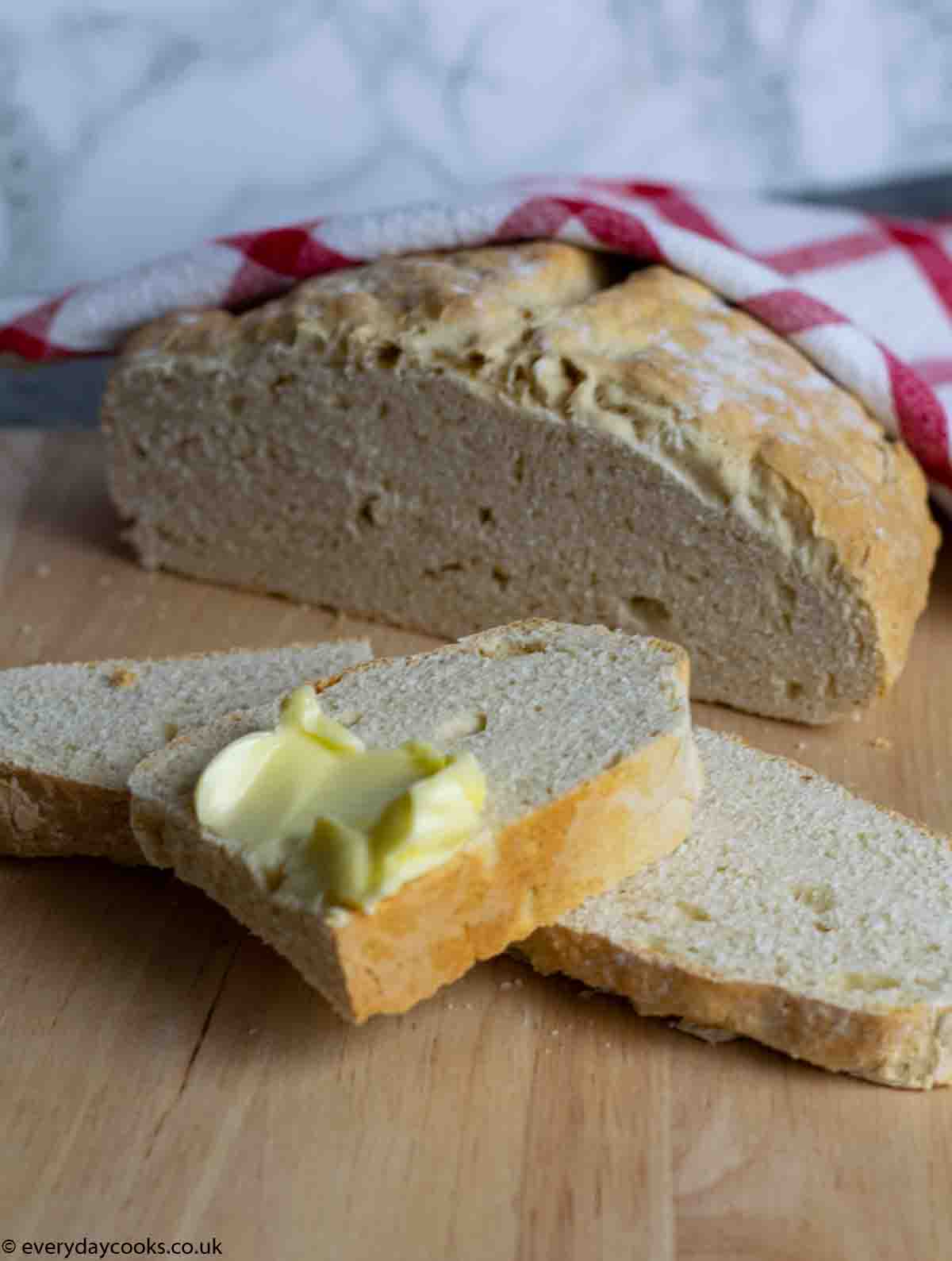 Half a loaf of Easy No Yeast Bread with 3 slices, butter on a beechwood board.