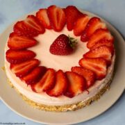 Easy Strawberry Cheesecake topped with sliced strawberries on a grey plate on a blue worktop.