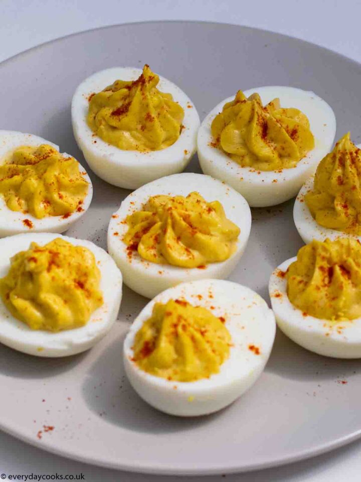 Eight Devilled Eggs halves, sprinkled with red paprika, on a grey plate