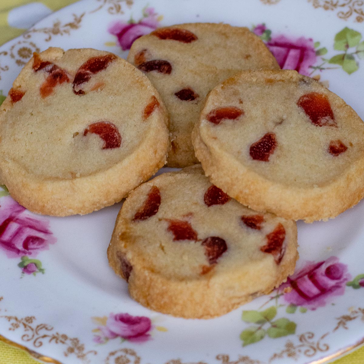 Four cherry shortbread biscuits on a pink and green patterned plate