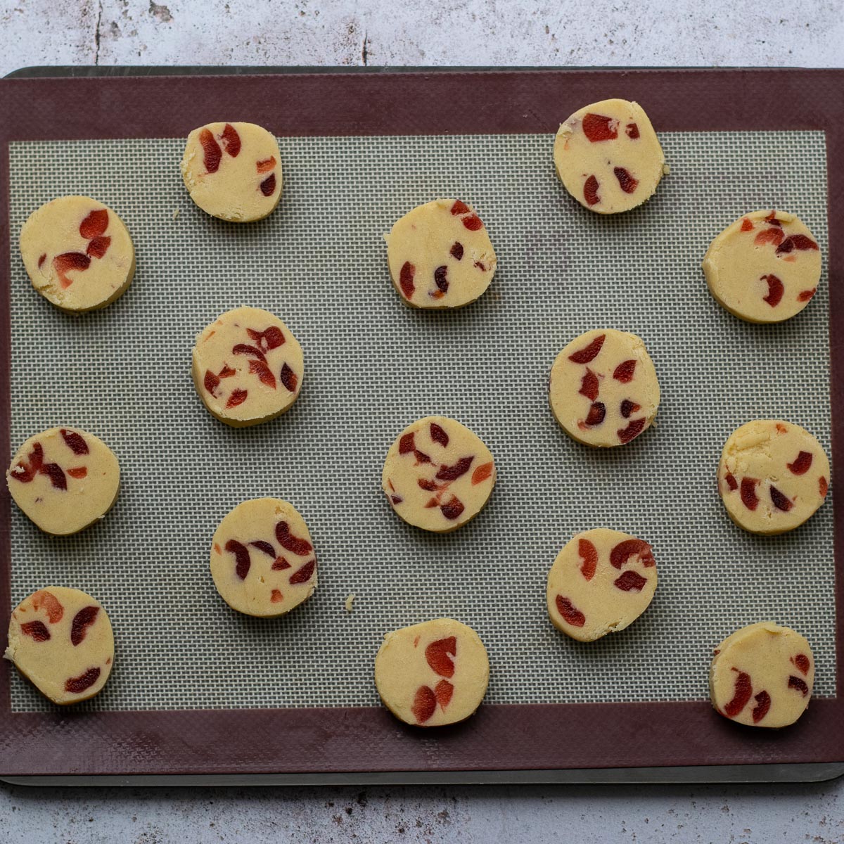 Slices of Cherry Shortbread dough on a baking sheet before cooking