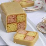 Easy Battenberg Cake on a white plate with 2 slices cut, with a cup of tea.