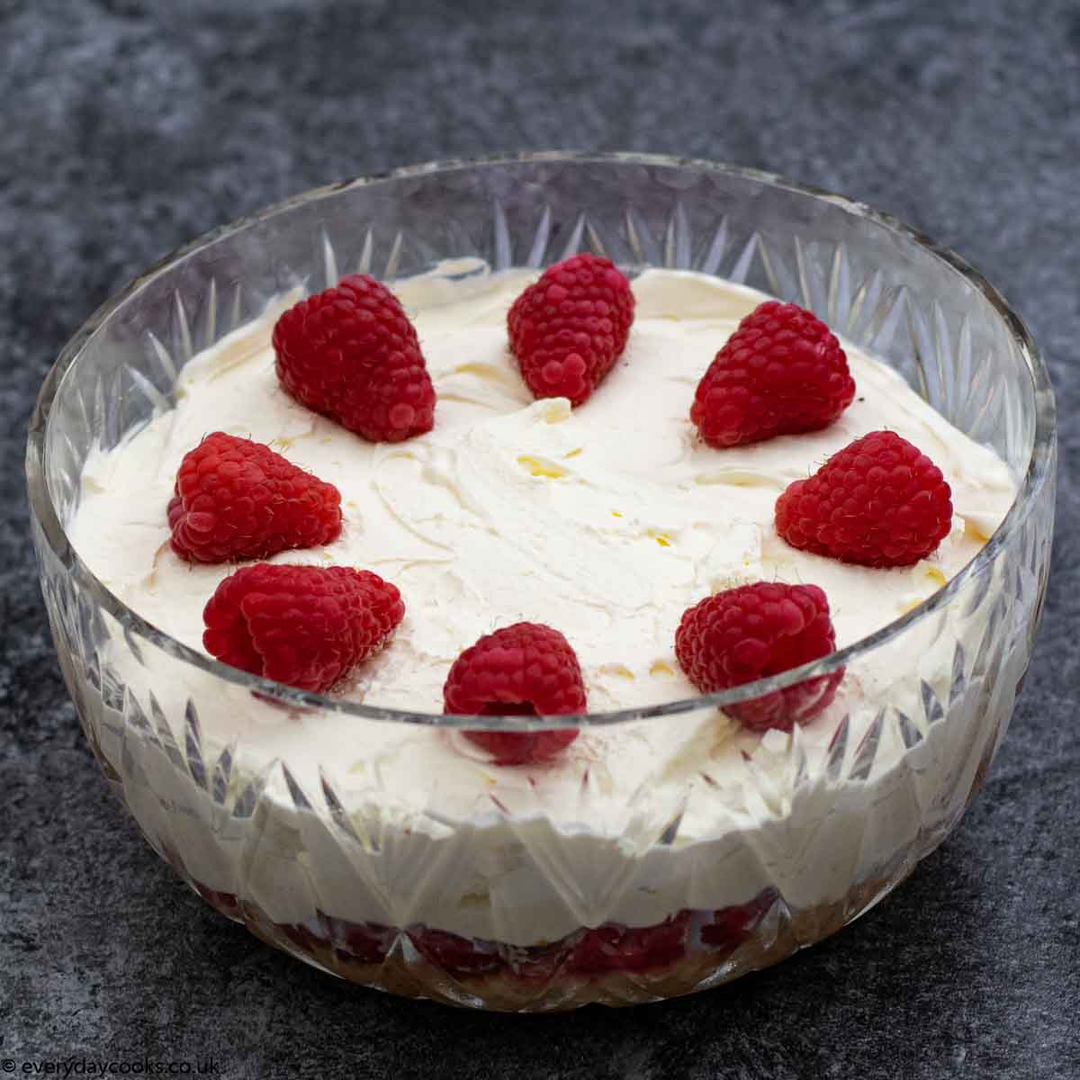 Sherry Trifle decorated with cream and raspberries in a crystal bowl on a dark worktop