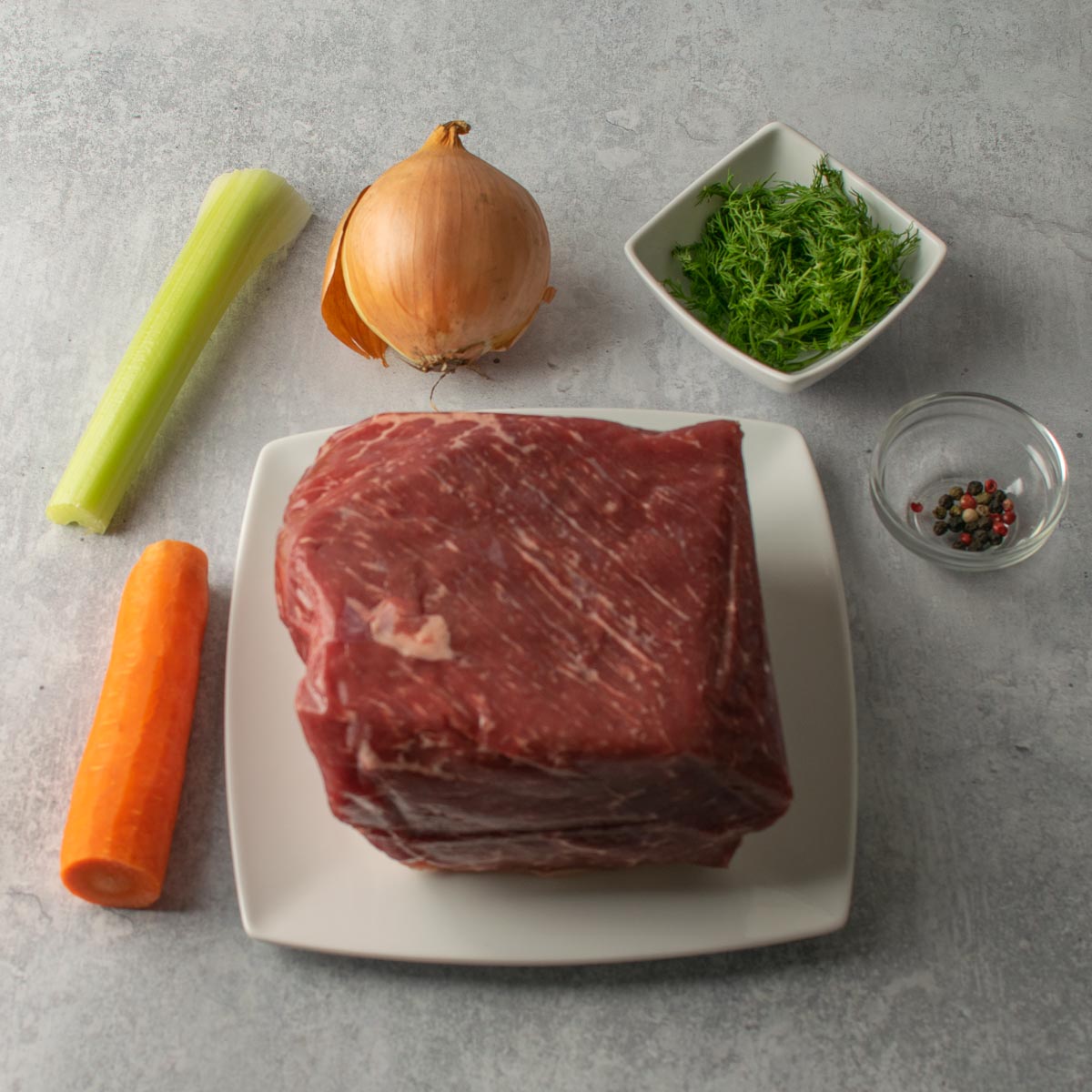 Ingredients for Slow Cooker Salt Beef: carrot celery stick, dill in a bowl, peppercorns in a bowl, joint of salt beef.