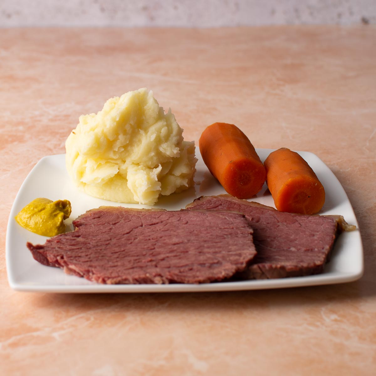 2 slices of Slow Cooker Salt Beef with carrots, mashed potato and mustard.