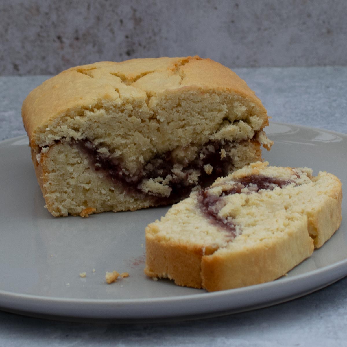 Half a Coconut Loaf Cake with jam filling with a slice cut on a grey plate