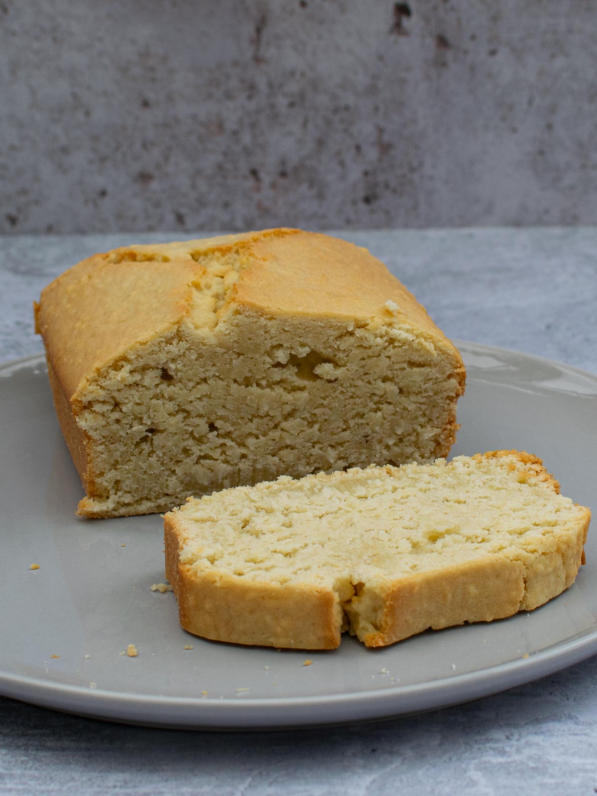 Half a Coconut Loaf Cake with a slice cut on a grey plate