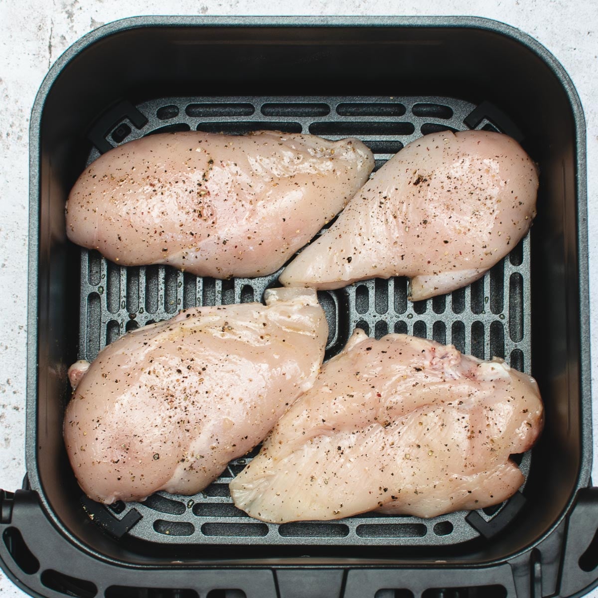 4 chicken breasts coated with oil and seasoned in the air fryer drawer.
