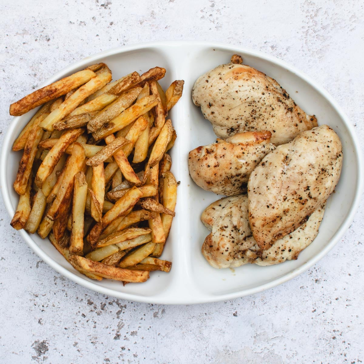 Air fryer chips and chicken breasts in a white, divided dish